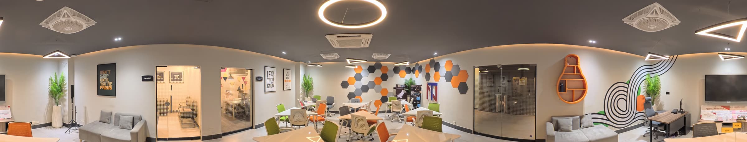 A 360° view of the NEIC coworking hall at NUTECH, Islamabad: hexagon feature wall, glass meeting rooms, desks and lounge seating.